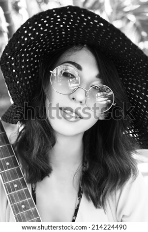 Sensual fashion portrait of young beautiful woman, hippie style round sunglasses and big hat, holding guitar. Black and white colors.