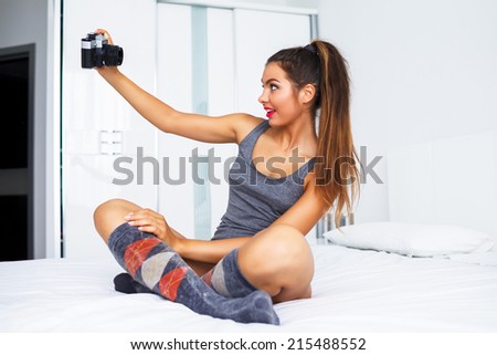 Pretty young fit tan girl making selfie on vintage camera, having fun in big light room, wearing cute pajamas,and ponytail, have great morning alone.