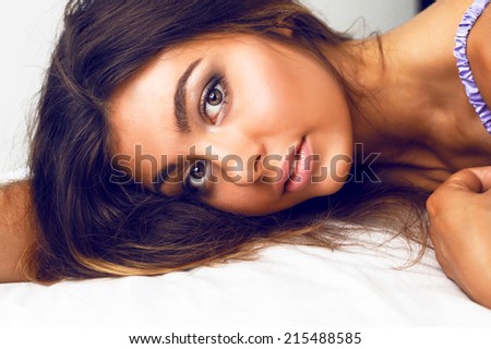 Close up sensual portrait of beautiful girl with perfect bronze skin big brown eyes and full lips laying at bed relaxing and enjoy morning time, have natural glow make up and  brunette long hairs.