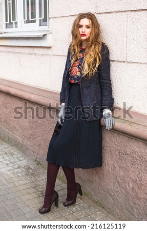 Outdoor fashion portrait of beautiful stylish girl posing at the street at elegant stylish coat dress and pumps, have long ginger hairs and perfect matched accessorizes .