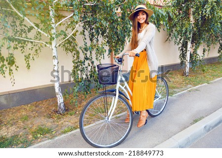 Young stylish elegant girl in maxi skirt warm jacket and straw hat, riding her hipster retro bike, enjoy nice sunny fall autumn day. lifestyle positive portrait of teenage pretty brunette girl.