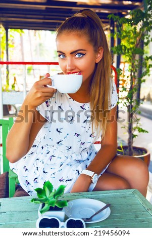 Outdoor fashion portrait of young pretty girl with beautiful big glue eyes, wearing pin up styled outfit and make up, enjoy her perfect morning with cup of coffee on shabby chic cafeteria terrace.