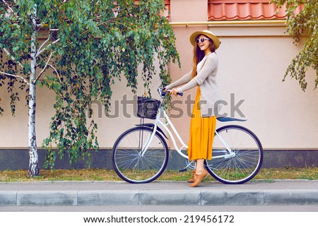 Outdoor fashion portrait of elegant lady riding her hipster retro bike in vintage stylish maxi skirt warm cardigan and straw hat. enjoy mica fall autumn day, posing at the street with birch trees.