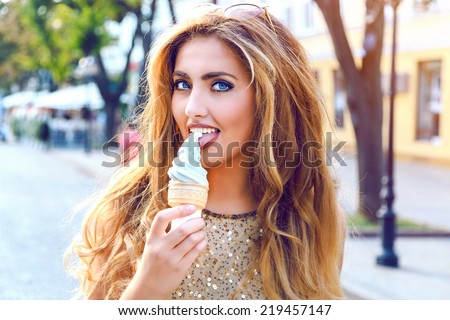 Closeup colorful fashion portrait of beautiful woman liking her favorite vanilla cone ice-cream, have gorgeous hairs, bright make up. walking alone at european city center at nice sunny fall day.