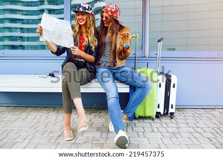 Two young pretty girls exploring and looking on map before their traveling adventures, smiling and having fun before new emotions. Best friend posing with their luggage.