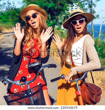 Two young pretty surprised girls, say you hello. Two best friends having fun together at park walk with retro bikes, wearing vintage clothes hats and sunglasses. Outdoor fashion portrait.