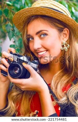 Close up fashion portrait of pretty blonde young woman with natural make up, wearing straw hat, holding vintage retro hipster old camera. Outdoors.
