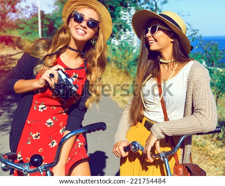 Outdoor fashion portrait of two hipster girls smiling laughing and have perfect free day together walking with retro bicycles taking pictures on retro camera wearing stylish vintage outfits Outdoor fashion portrait of two hipster girls smiling laughing and have perfect free day together walking with retro bicycles taking pictures on retro camera wearing stylish vintage outfits