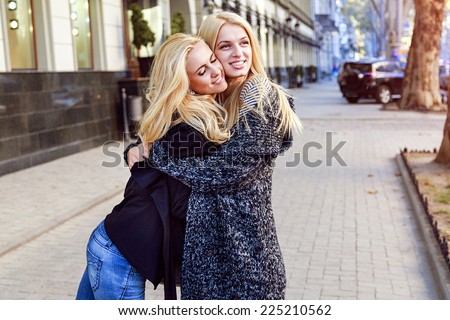 Outdoor image of two pretty best friends blonde girl hugs on the street. Fashion portrait of two stylish blonde sisters.