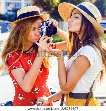 Close up fashion portrait of two funny young pretty blonde and brunette sisters, making funny pictures on retro vintage camera, two stylish best friends having fun together.