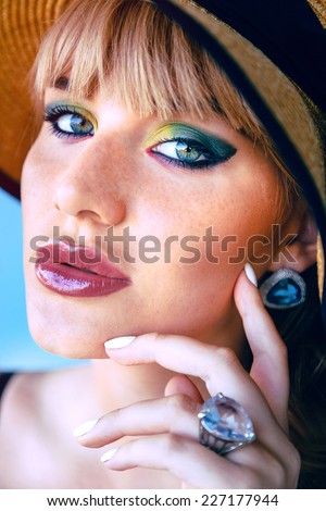 Close up fashion portrait of young woman with freckles big green eye and full lips, wearing bright colorful make up,  jewelry and straw hat.