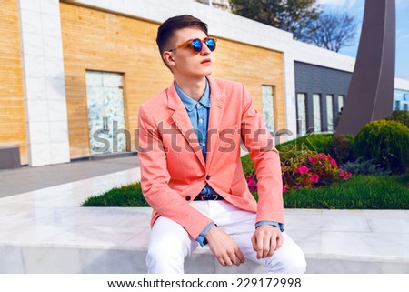 Young stylish handsome man posing in modern city park and shopping mall, wearing stylish bright outfit and sunglasses, dandy look.