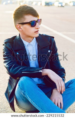 Fashion outdoor urban portrait of young stylish handsome guy wearing jeans sunglasses and leather biker jacket.