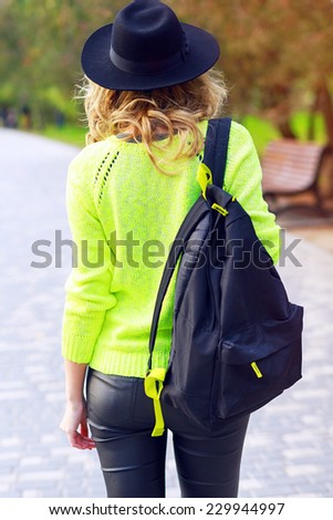 Fashion image of woman posing at trendy leather pants, neon green sweater, backpack and vintage hat. Fall portrait of young stylish traveller backpacker girl.