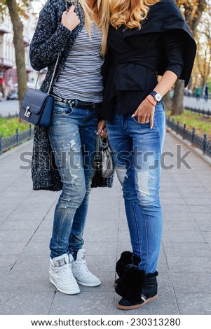 Outdoor fashion portrait of two stylish girls wearing trendy fall autumn outfits, cozy jackets denim and sneakers. Street style look.