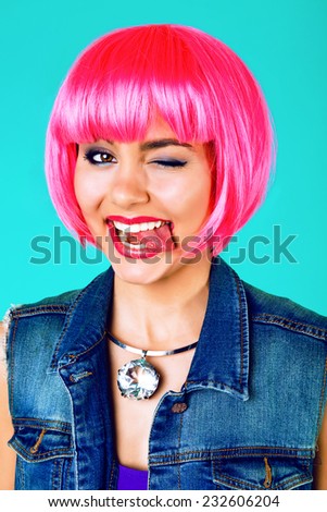 Close up fashion studio portrait of pretty young cheerful positive woman wearing bright make up and neon pink party wig, winked and showing tongue. Bright sweet colors.