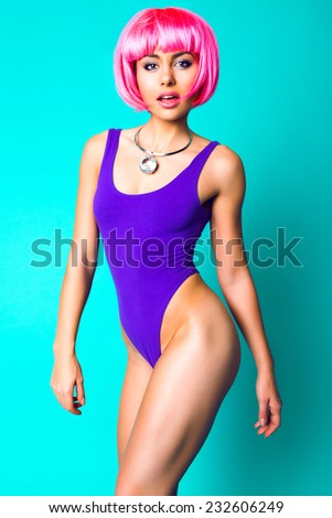 Fashion studio portrait of fitness model with perfect skin and body wearing sportive swimsuit carnival pink wig and massive diamond necklace. Gorgeous fit woman, bright sweet colors.