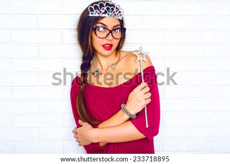 Indoor fashion lifestyle positive portrait of young sexy brunette hipster woman, ready for masquerade party wearing  fairy costume funny fake crown and magic wand.Bright colors, brick wall background.