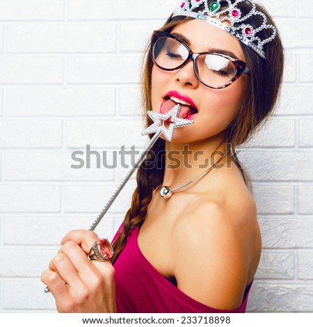 Close up funny portrait of brunette hipster woman, ready for masquerade party wearing sexy fairy costume, stockings, vintage glasses, funny fake crown and liking magic wand .