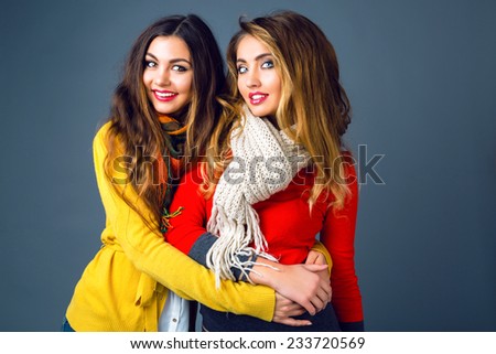 Fashion winter portrait of blonde and brunette beautiful best friends girls, hugs and having fun. Wearing bright stylish cashmere sweaters and scarfs. Have trendy make up and long amazing hairs.