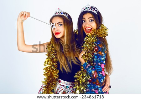 Portrait of beautiful women friends wearing bright sexy outfits, funny fake crowns  tinsel and magic want, ready for celebrating holidays party. having fun together screaming and making funny faces.