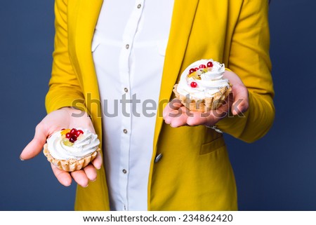 Close up portrait of  woman in classic yellow blazer with holding two tasty cakes with berries and cream.