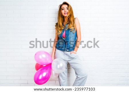 Indoor image on young trendy hipster blonde woman playing with pink balloons, ready for party. Urban white background, positive emotions.