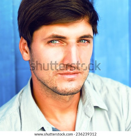 Close up portrait of young handsome man wearing casual shirt with green eyes, blue wooden background.