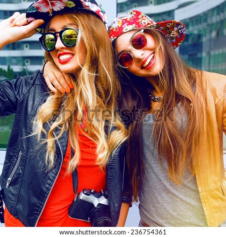 Lifestyle fashion portrait of happy stylish girls friends, hugs and enjoy travel time together, wearing hats and sunglasses holding vintage retro camera, bright colors positive emotions.