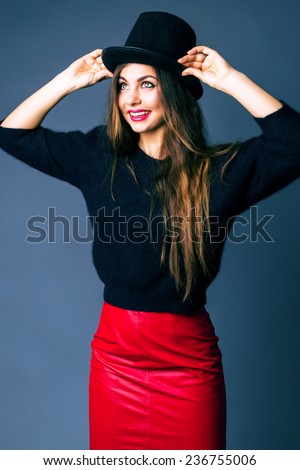 Studio fashion portrait of stylish woman with amazing long hairs wearing unusual cylinder hat black sweater and sexy leather red skirt.
