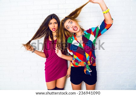 Lifestyle i,age of two young friend girls making crazy funny faces, wearing bright hipster clothes, urban white background.