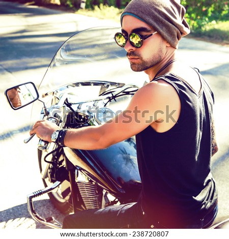 Young handsome stylish man riding bike, wearing hat and sunglasses, brutal rock n roll style. Instagram bright colors.