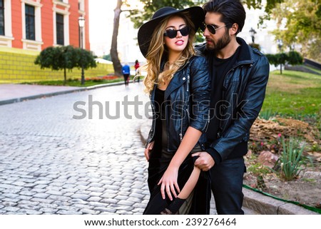Young pretty couple in love hugs on the street of old town, wearing stylish total black leather rock n roll clothes and sunglasses. Outdoor fashion portrait of lovers.