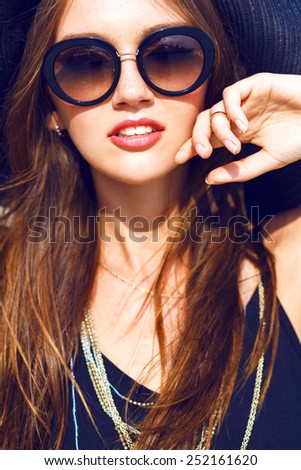 Close up fashion portrait of sexy stylish young woman wearing total black look, retro sunglasses and hat, have perfect skin and amazing long brunette hairs.