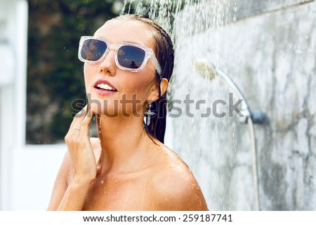 Young sexy blonde girl with beautiful face and perfect skin get tropical shower, enjoy her summer vacation, wearing stylish sunglasses and jewelry.