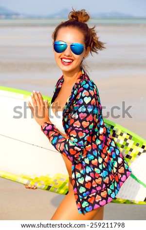 Close up fashion lifestyle summer portrait of stunning sexy surfer woman, wearing bright outfit makeup and sunglasses. Holding surf board s,killing and having fun alone.