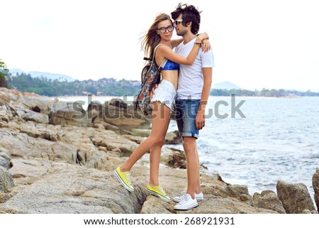 Young hipster couple in love travel together in summer time, posing at amazing beautiful stone beach, wearing stylish casual outfits, hugs and having fun.