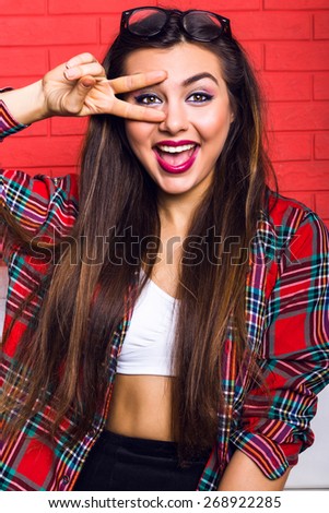 Fashion bright portrait of young woman with amazing long hairs and bright make up,having fun at the room, wearing hipster outfit, red urban wall background.