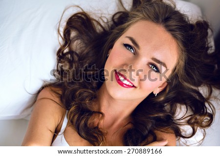 Tender fashion morning portrait of stunning young sexy woman with freckles fluffy hairs and bright make up, lay and relax on the bed, cute smiling positive face and emotions, soft colors.