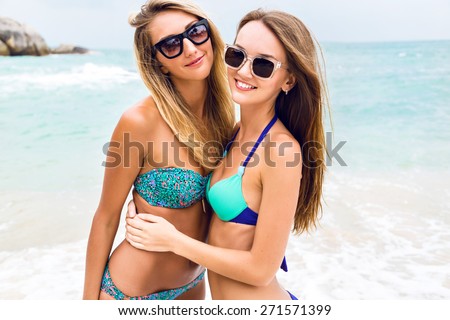 Two young sexy stunning women walking  having fun smiling hugs and looking on camera at paradise beach. Fashion summer portrait go girls in bikini enjoy their exotic vacation.