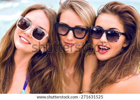 Close up lifestyle portrait of thee young stunning women with long hairs perfect skin and bright bikinis, posing on the beach at nice sunny summer day, having great time together.