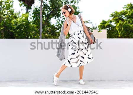 Outdoor summer lifestyle fashion portrait of young hipster stylish woman walking on the street, wearing vintage clothes and earphones, clear fresh colors.