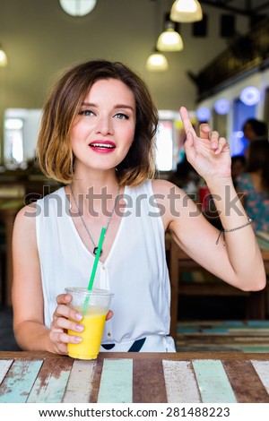Beautiful woman asking for waiter in restaurant, put her hand to the air, drinking fresh healthy mango juice, bright sexy make up.