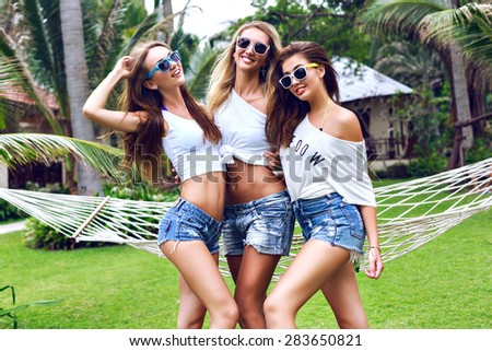 Fashion summer portrait of tree young sexy pretty woman, wearing simple casual trendy white tops, mini denim vintage shorts and bright sunglasses, smiling having fun on vacation in tropical country.
