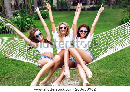 Summer lifestyle portrait of tree girls going crazy, screaming, laughing having fun together, jumping at hammock.  wearing white tops and sunglasses, ready for party,  joy, fun.