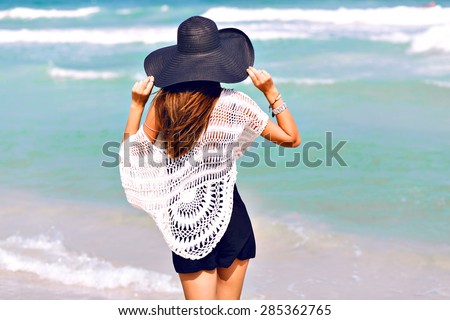 Summer fashion portrait of amazing fit sexy woman posing in the front of blue ocean on tropical hot exotic island, wearing romper and vintage hat, bright colors,joy, vacation.