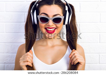 Favorite music, good mood. The girl in sunglasses and headphones listening to music with the hands holding  the hair tied in a ponytail, white background. Crazy disco style.