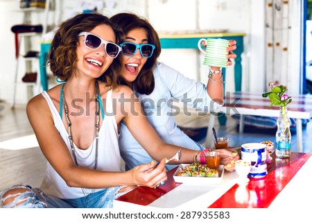 Two pretty best friend girls enjoy their lunch together in cute cafe, smiling speaking and gossip, bright clothes sunglasses, jewelry and accessorizes. portrait of women taking breakfast .