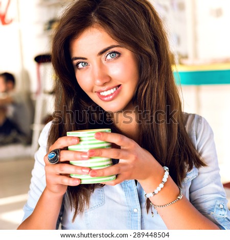 Close up indoor portrait of young pretty brunette woman, drinking morning coffer in cafe, fresh natural make up and long hairs, cute smile, fun, joy.