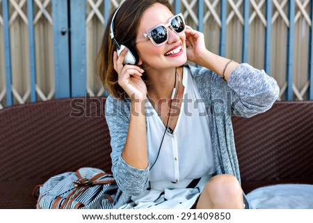 Young pretty woman sitting in the beach wearing stylish casual vintage styled outfit, relaxed and listening music, bright sunny colors, joy, amazing weekends.